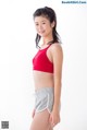 A young woman in a red sports bra top and gray shorts.