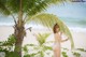 A woman in a bikini standing next to a palm tree on the beach.