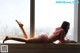 A woman laying on a window sill in front of a window.