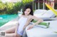 A woman in a white bathing suit sitting on a lounge chair by a pool.