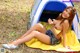 A woman sitting on a yellow blanket in front of a tent.