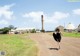 A woman in a black dress is walking down a dirt road.