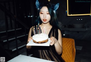 A woman holding a birthday cake with lit candles.
